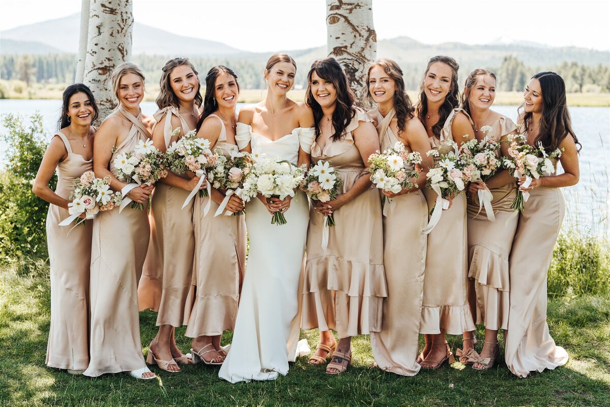 Bridal party in mismatched champagne dresses holding dainty wildflower bouquets with cosmos at Black Butte Ranch