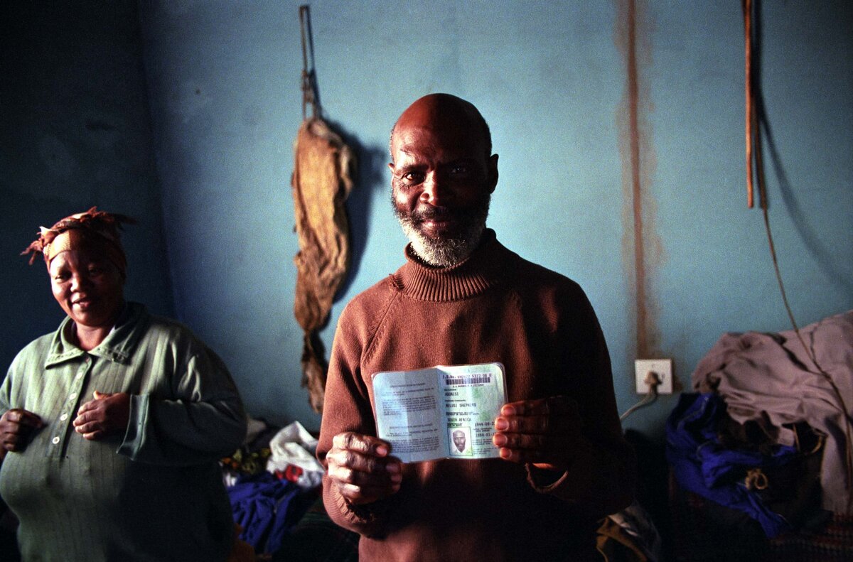A man from South Africa in rural village shows passbook with women in background. Social Documentary Editorial Photo