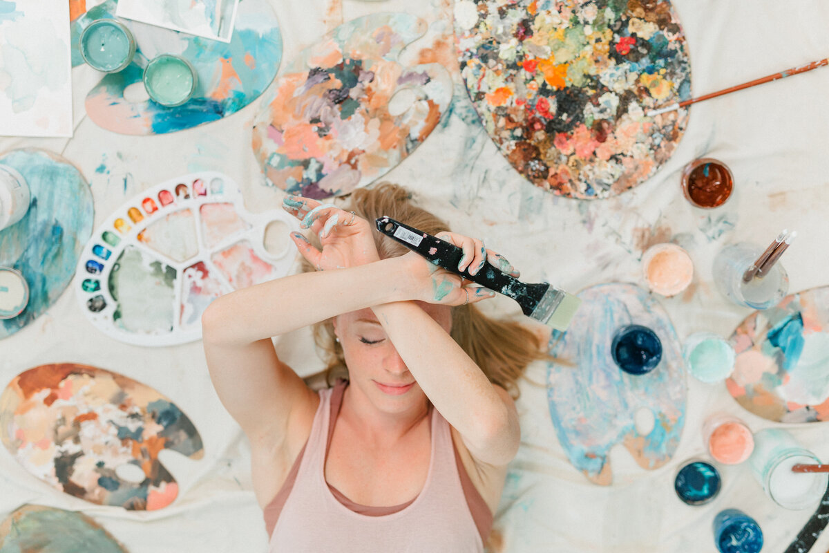 Caitlyn Mary Art, abstract artist, lying down with her paints; by Ariana del Mundo Photography