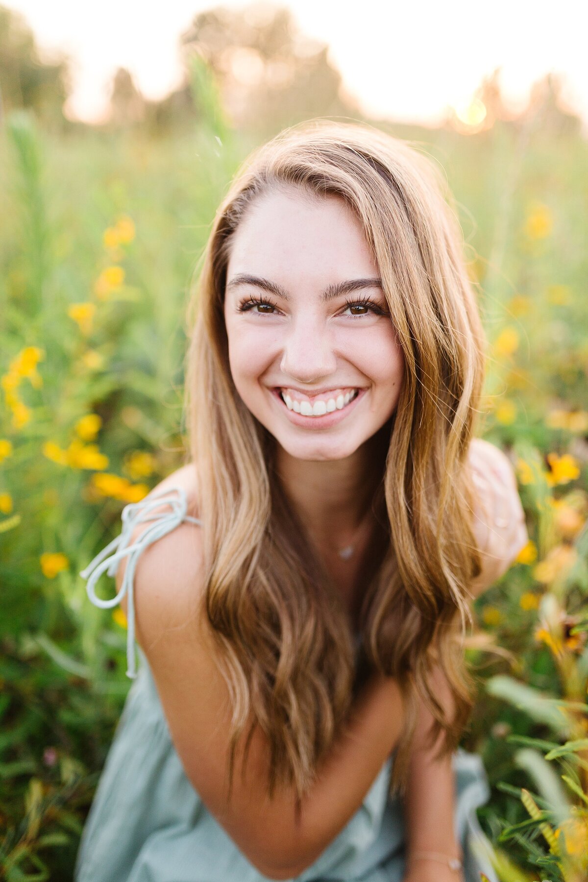 A high school senior girl, sitting in a field of flowers at sunset in Lexington KY.