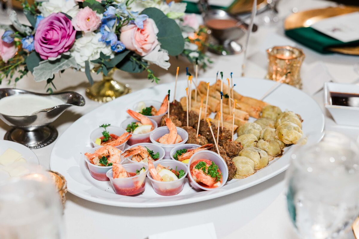 Elegant banquet table displaying a variety of appetizers including shrimp cocktails, meatballs, and stuffed dumplings, surrounded by floral arrangements at a park farm winery wedding.