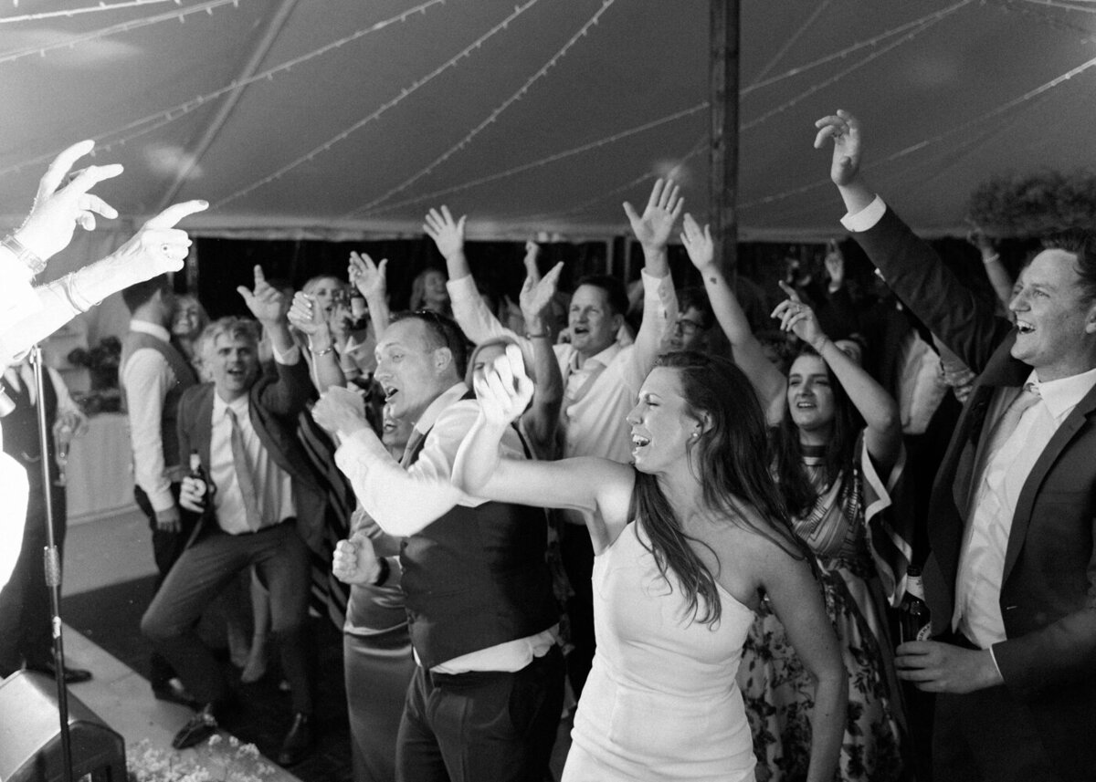 black and white photo of wedding guests dancing with raising hands and wedding band singing