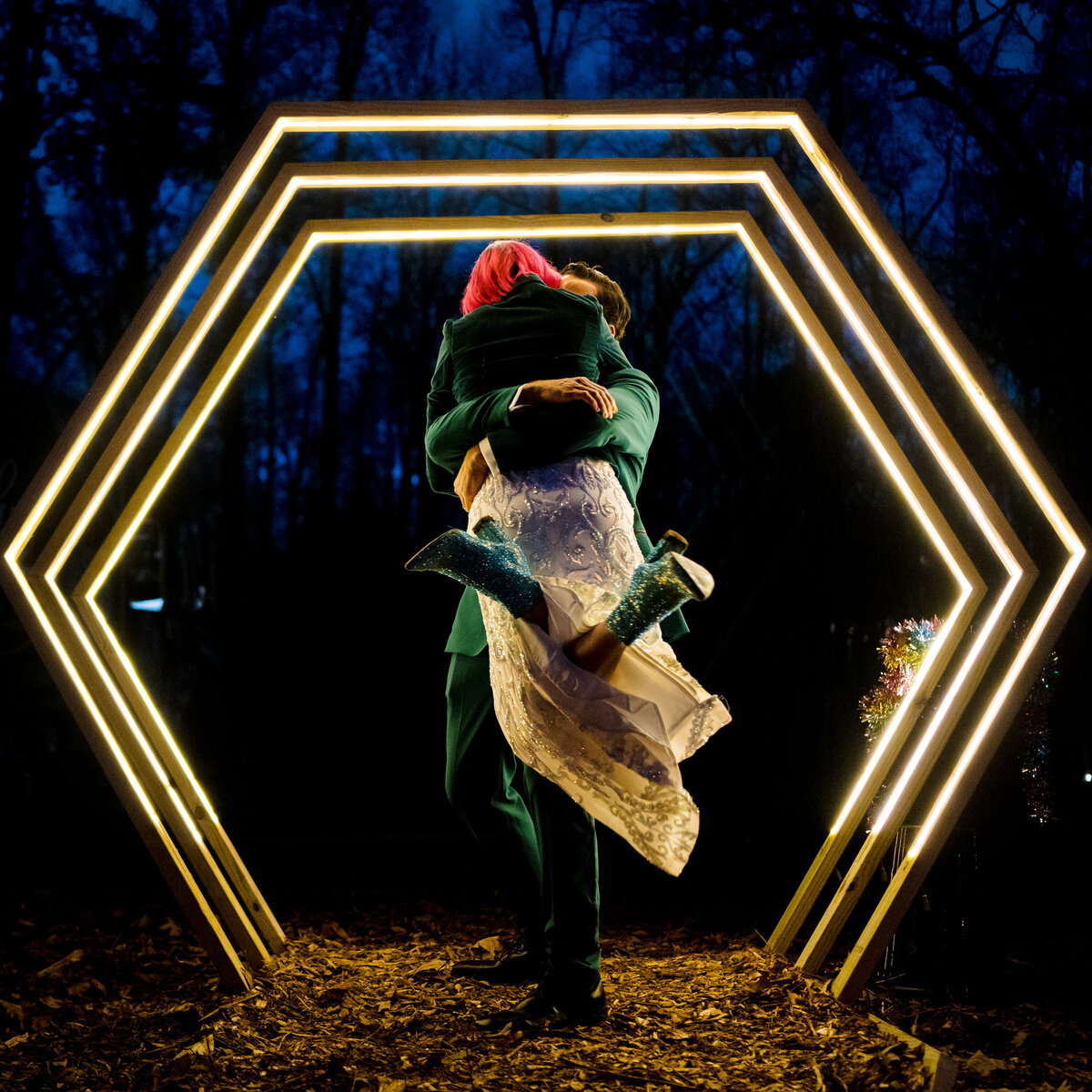 A person lifting their partner off the ground as they hug under a hexagon shaped light.