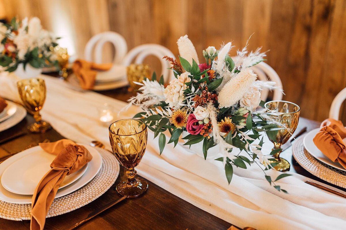 table centerpiece with ivory, greenery, and rust colored  flowers