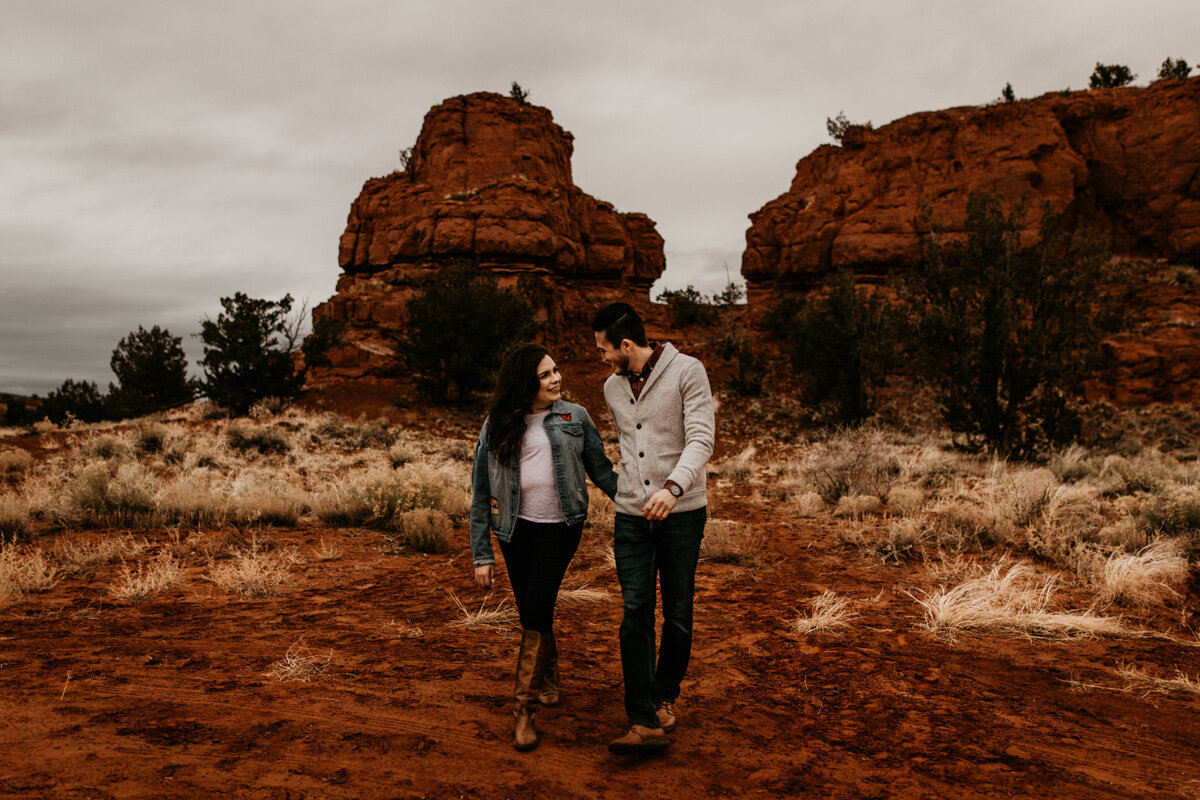 engaged couple walking in front of red rocks