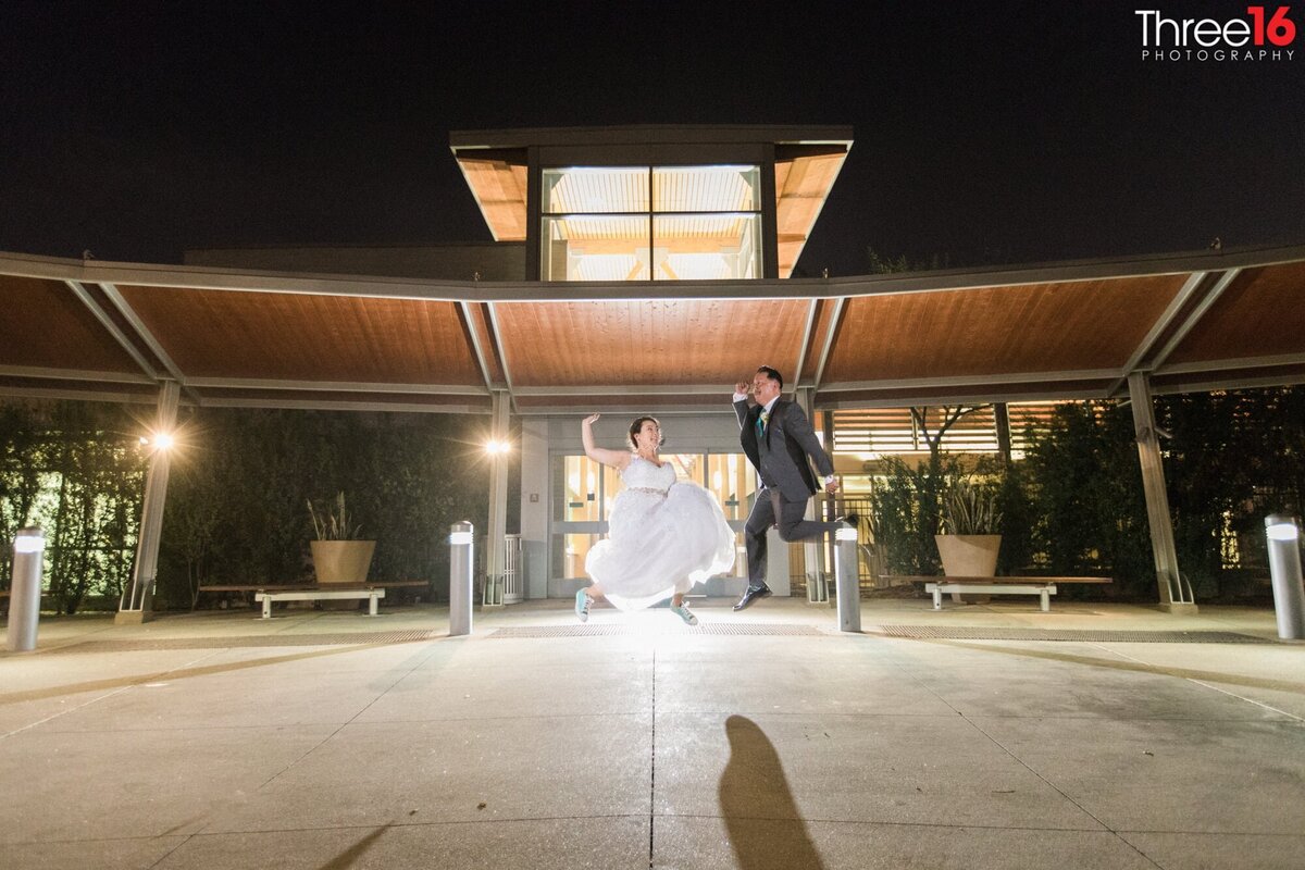 Bride and Groom jump for joy during a night shot in front of the Fullerton Community Center