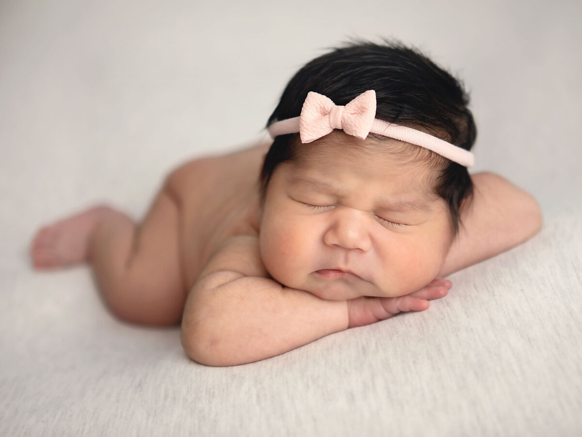 newborn-sleeping-on-her-arms-with-a-head-band-while-doing-her-newborn-shoot