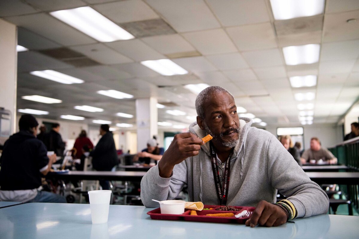 Editorial portrait of a man eating with tray of food at Father Joe's Soup Kitchen