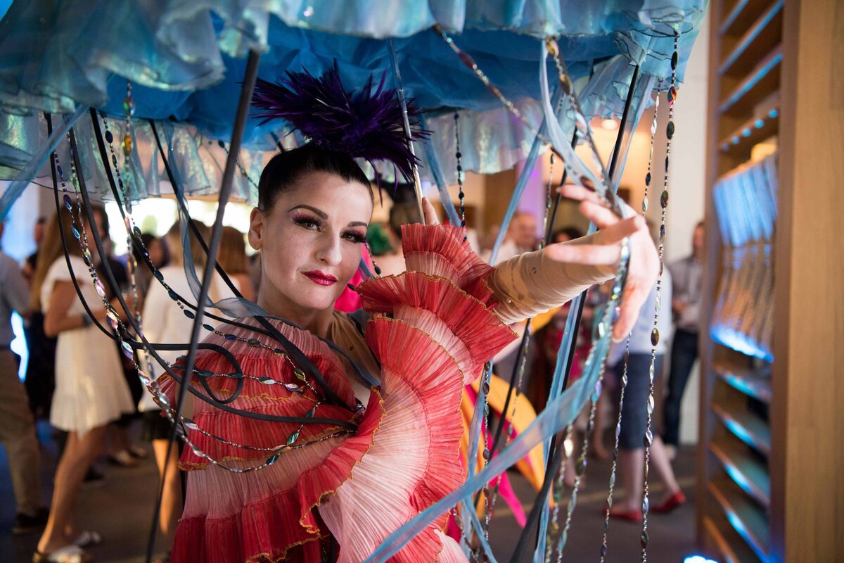 A dancer with umbrella, costume and face painted roams a meeting as guests mingle and take photos with her.