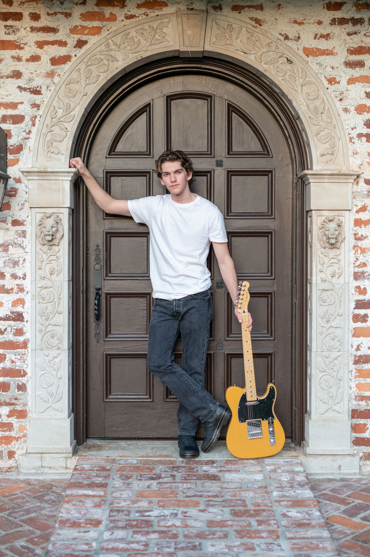 High school senior boy leans in doorway with guitar.