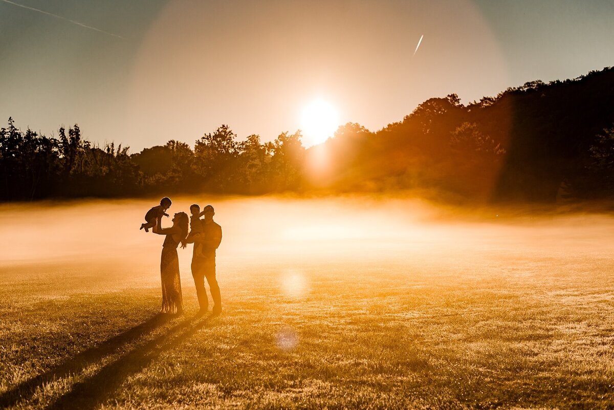 beautiful lifestyle shot of family at sunrise with fog standing together in a field showing connection with gorgeous light and moment image by Huntersville Photographer