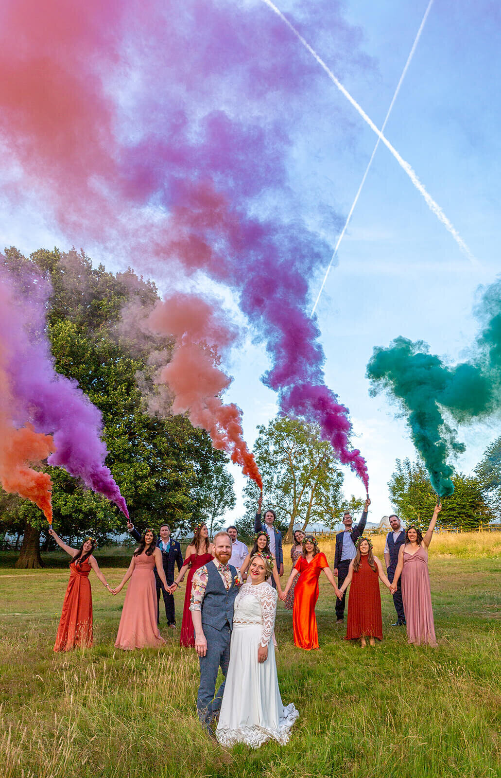 Bride and groom stand in field with wedding party and colour bombs