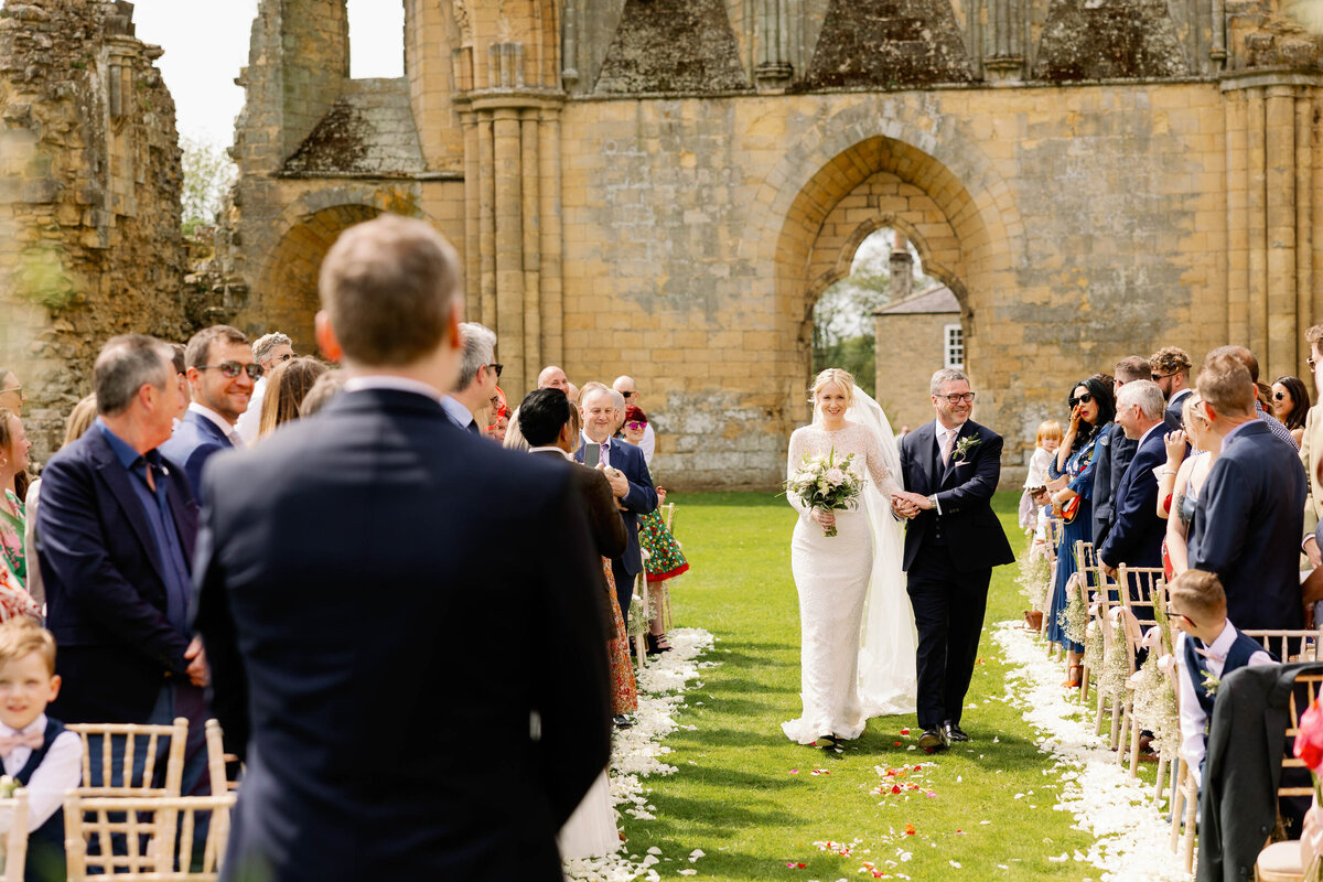 Bride walking up the aisle for her outdoor ceremony at Byland Abbey