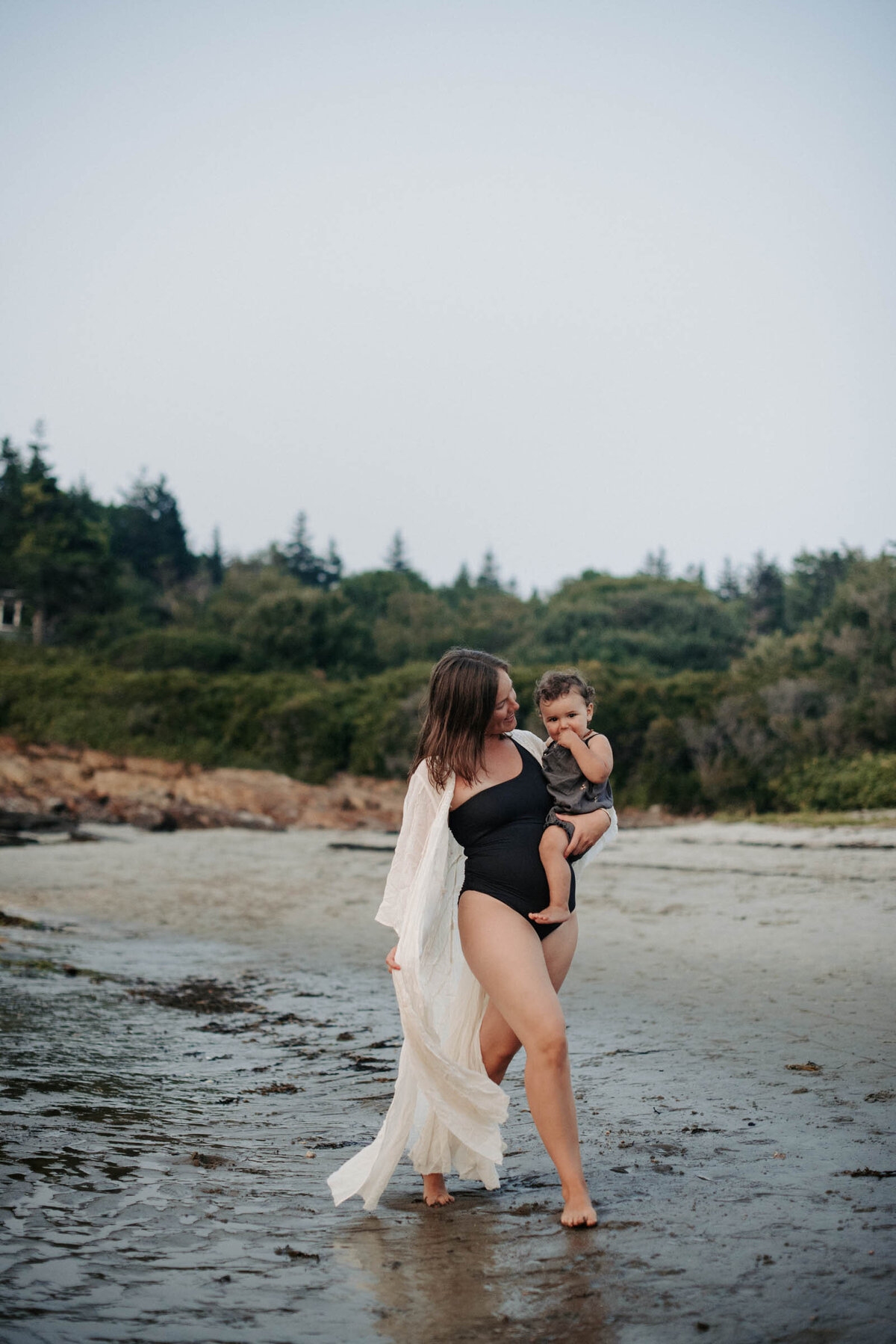 A mother walks on the beach holding baby Maine