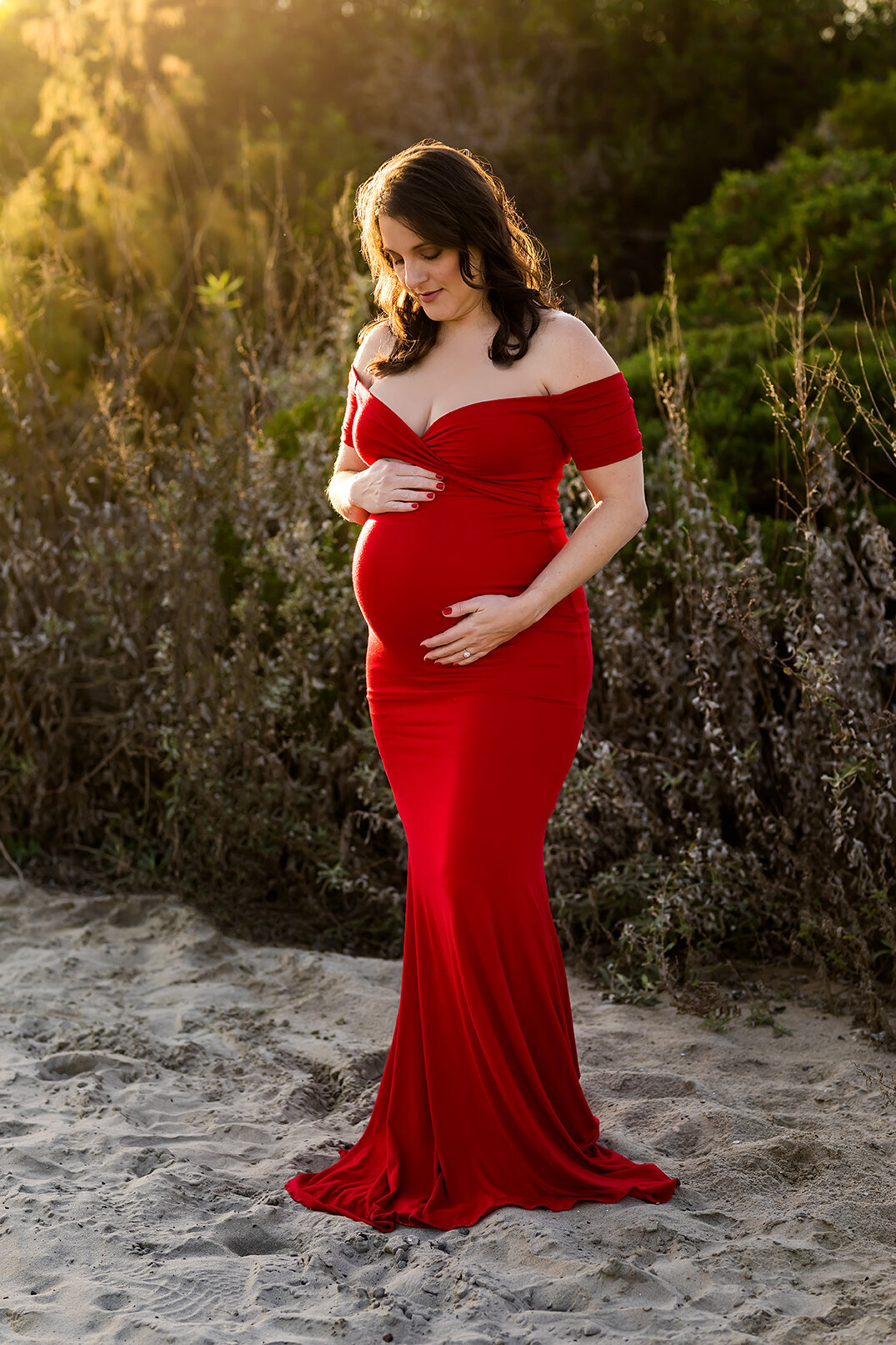 Portrait of pregnant woman in red gown on the beach in Carlsbad