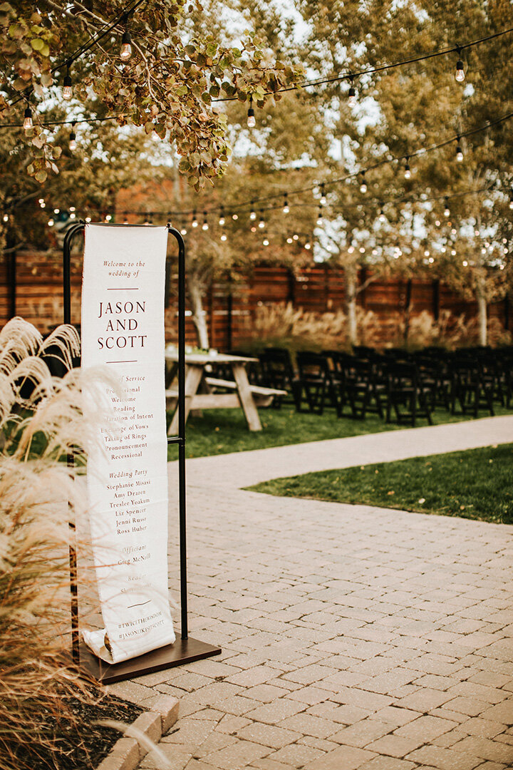 White wedding banner with black font hanging on black metal stands in quart yard.