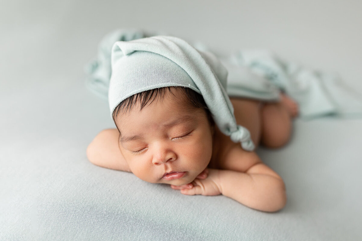 Newborn boy wearing a blue sleepy hat posed for his newborn session.