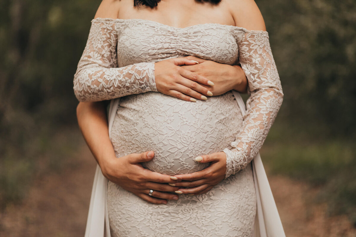 mom wears beige maternity dress with dads hands wrapped around her belly