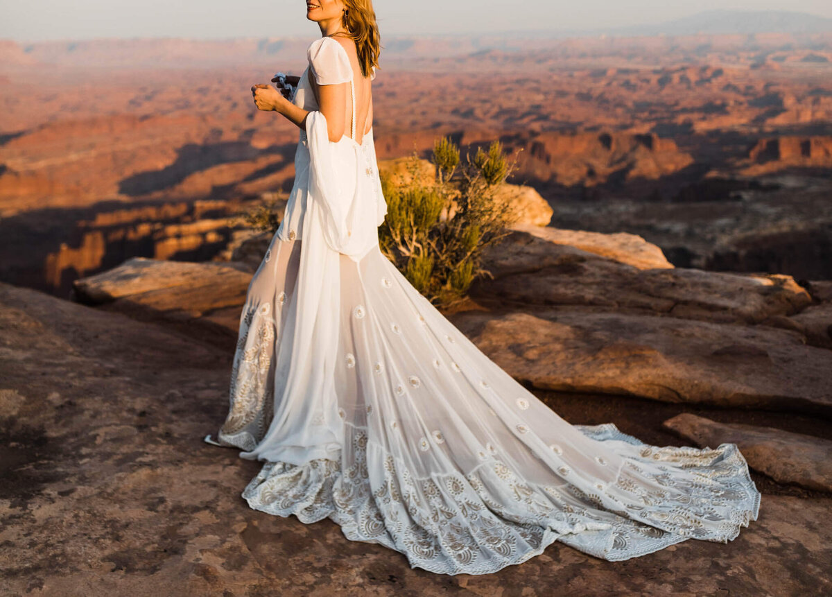 the boho bride sits in a slot canyon and laces her boots. her lace dress fans out beside her.