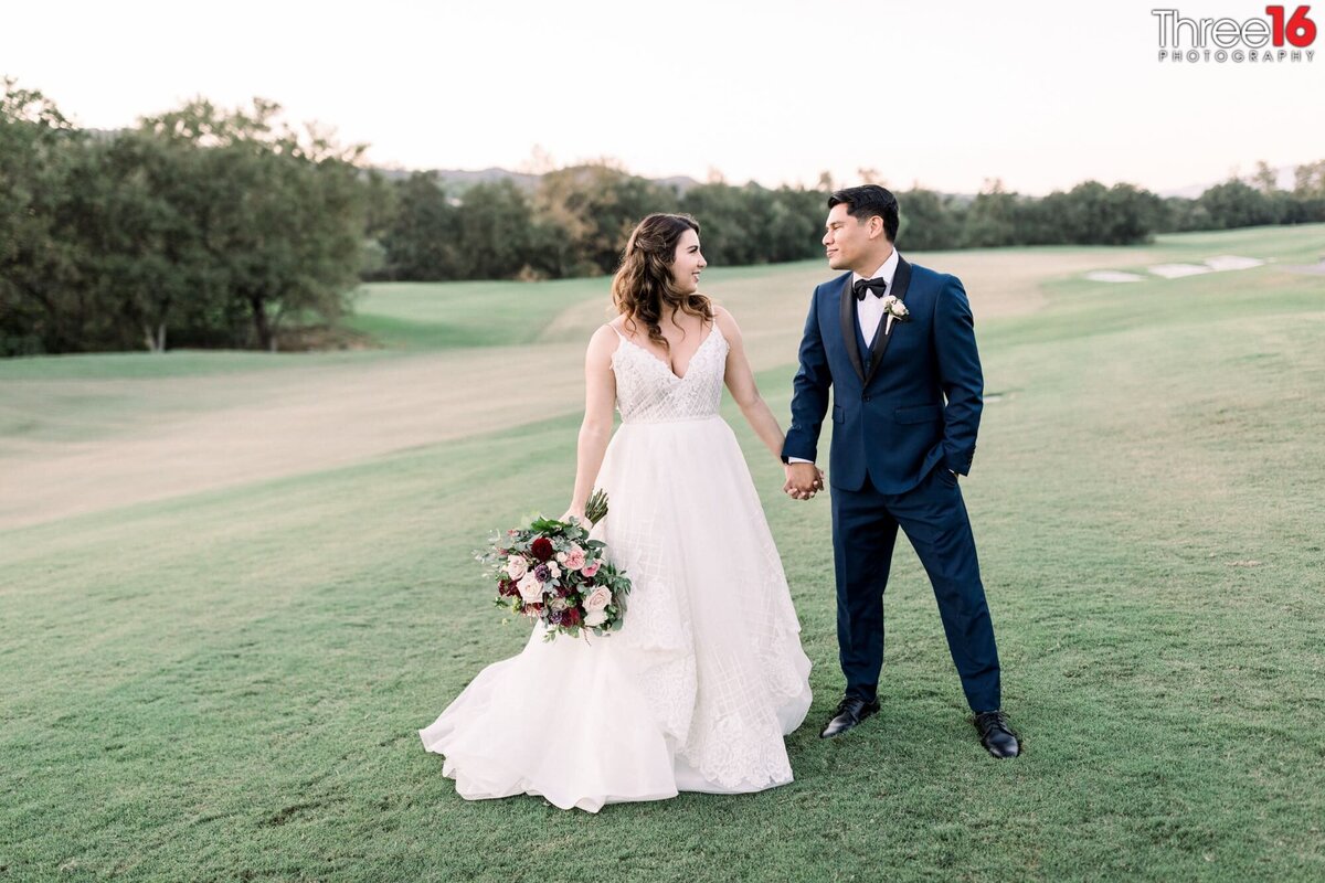 Bride and Groom hold hands as they look at each other during photo session on the golf course
