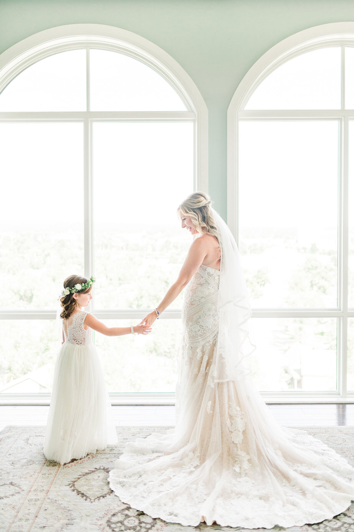 A bride holding her flower girl's hand in front of a window at the Pinery at the Hill in downtown Colorado Springs.