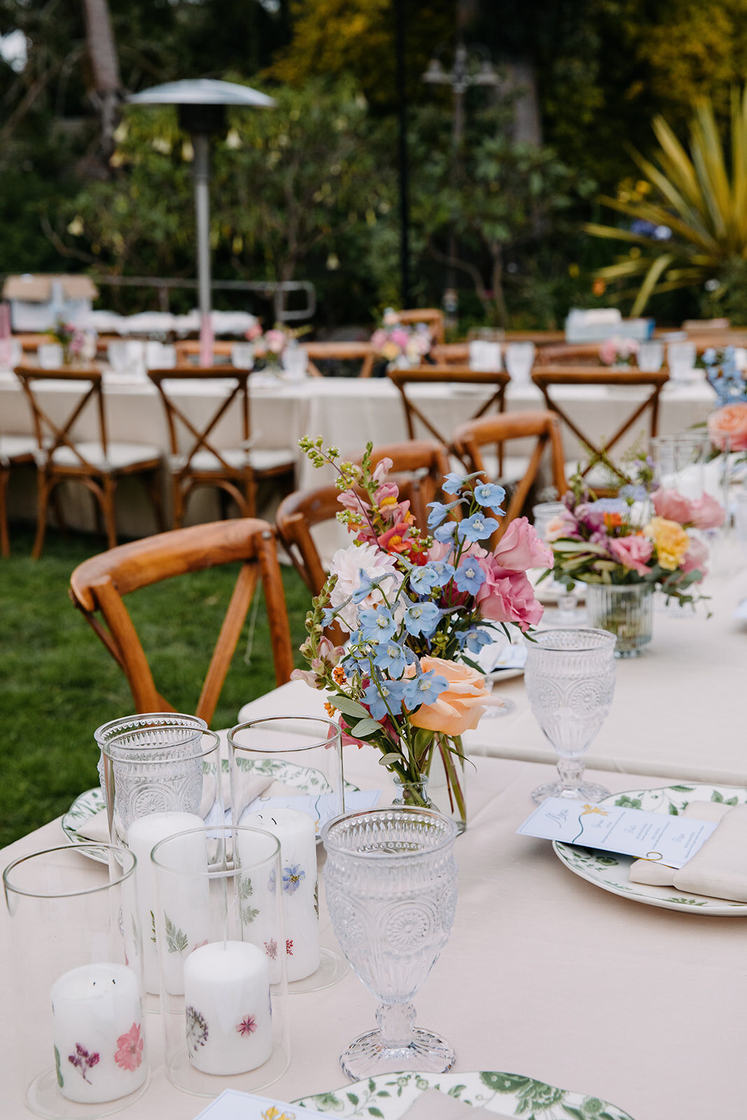 Outdoor garden table setting with clear glassware and colorful floral arrangements.