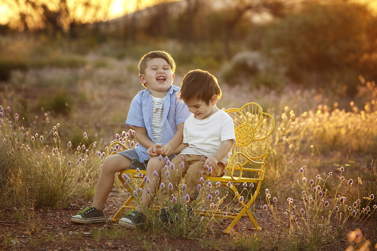 Two boys sitting on yellow chair in a field with golden sunlight
