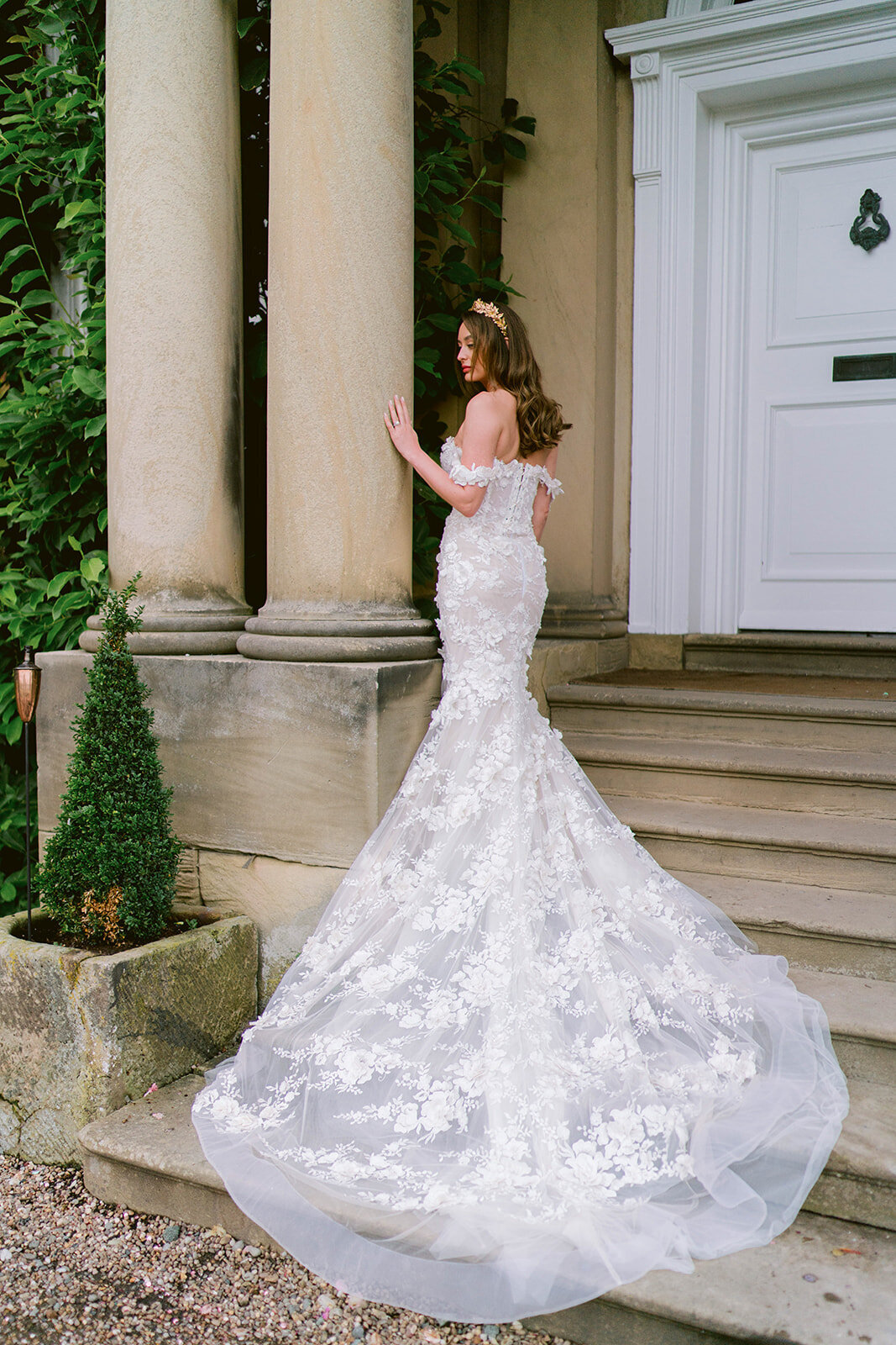 A beautiful bride is wearing a Galia La hav wedding dress on the stairs of Iscoyd park at the front of the house
