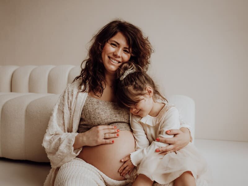 Intiem beeld van zwangere mama met oudste kindje dat liefdevol de buik streelt.