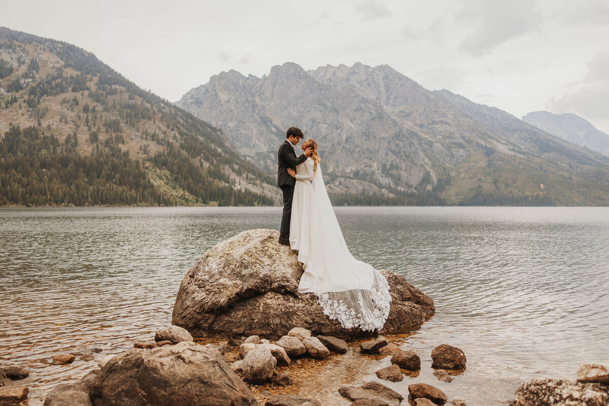 brie and groom embracing on large rock in lake