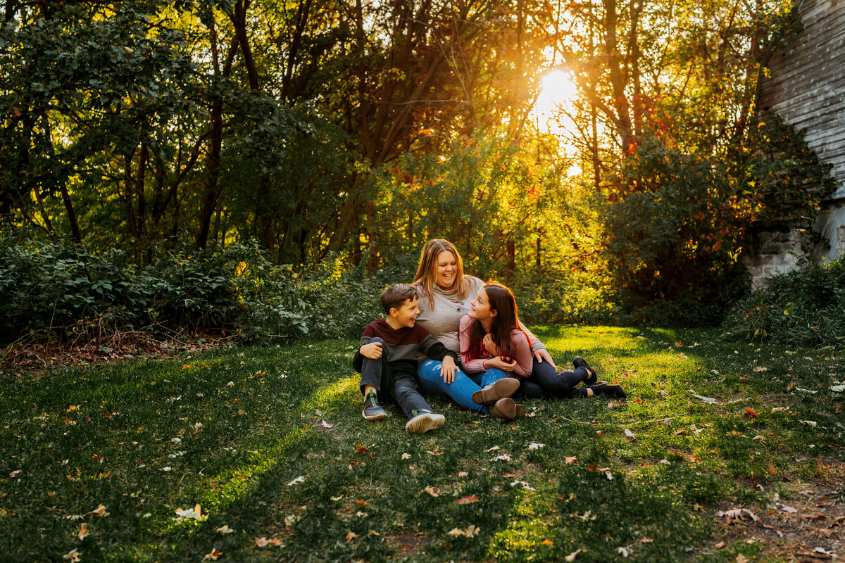 family of three at sunset sitting on blanket in grass