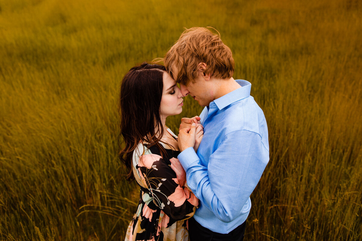 a romantic engagement photo in downtown Toledo Ohio. The couple snuggles together in a grass field at Middle grounds metropark.  Photo By Adore Wedding Photography. Toledo Wedding Photographers