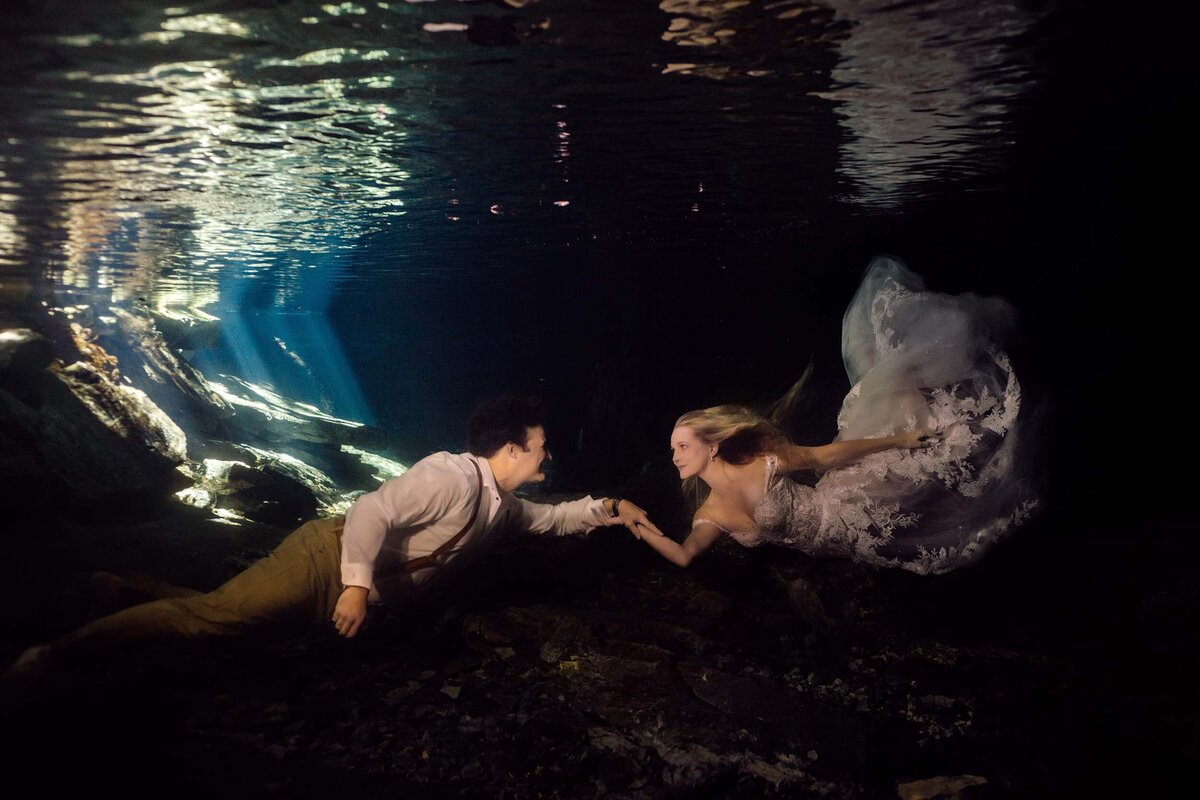 Bride and groom reach for each other underwater during Trash the Dress in Riviera Maya