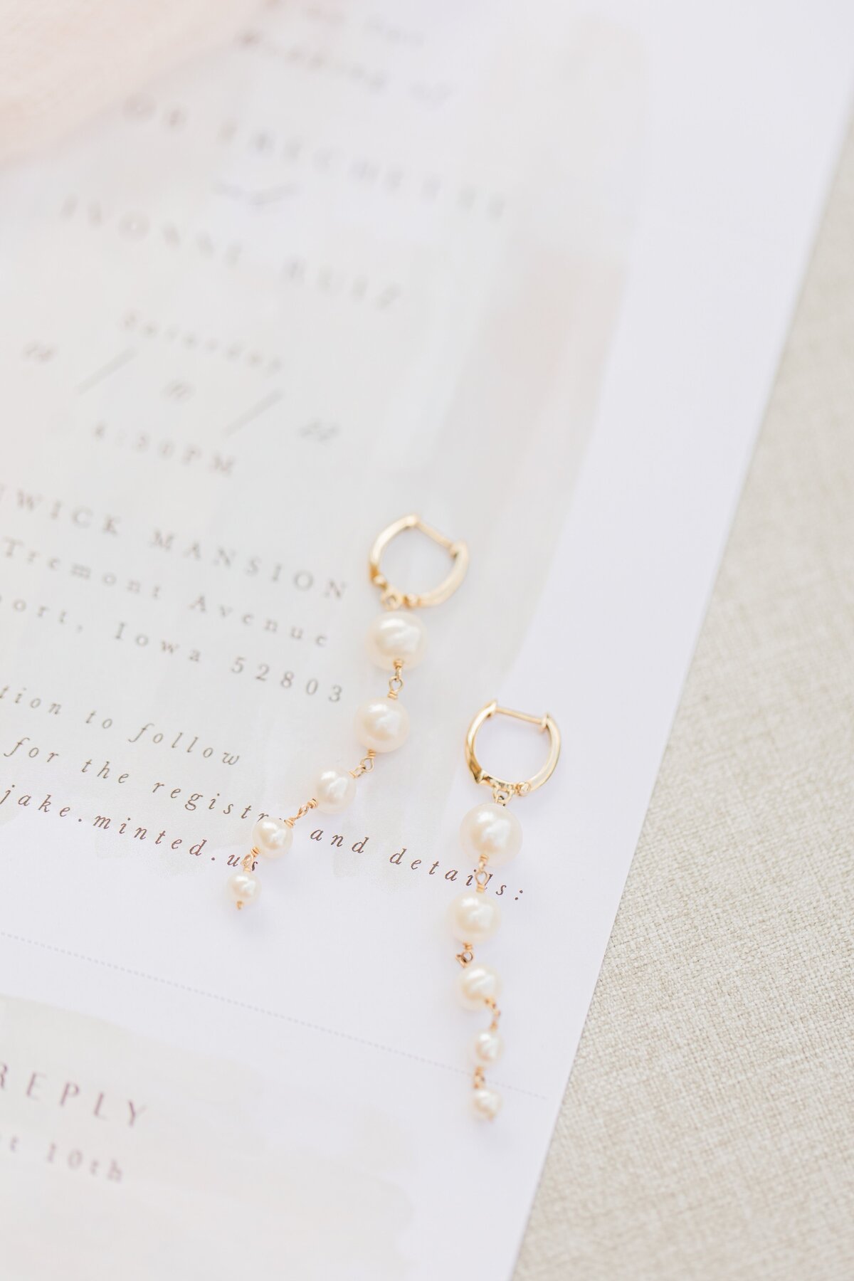 Elegant gold earrings with pearl accents displayed on an Iowa wedding invitation with cursive text.