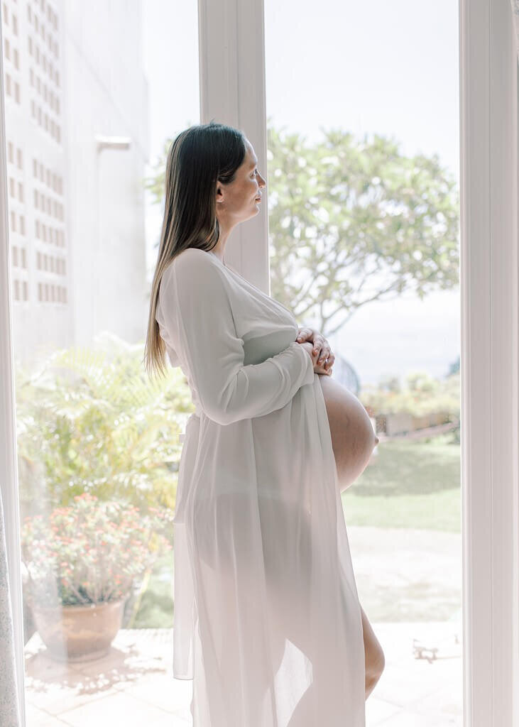 Soon to be mommy in a see through maternity coverup gazing out the window.