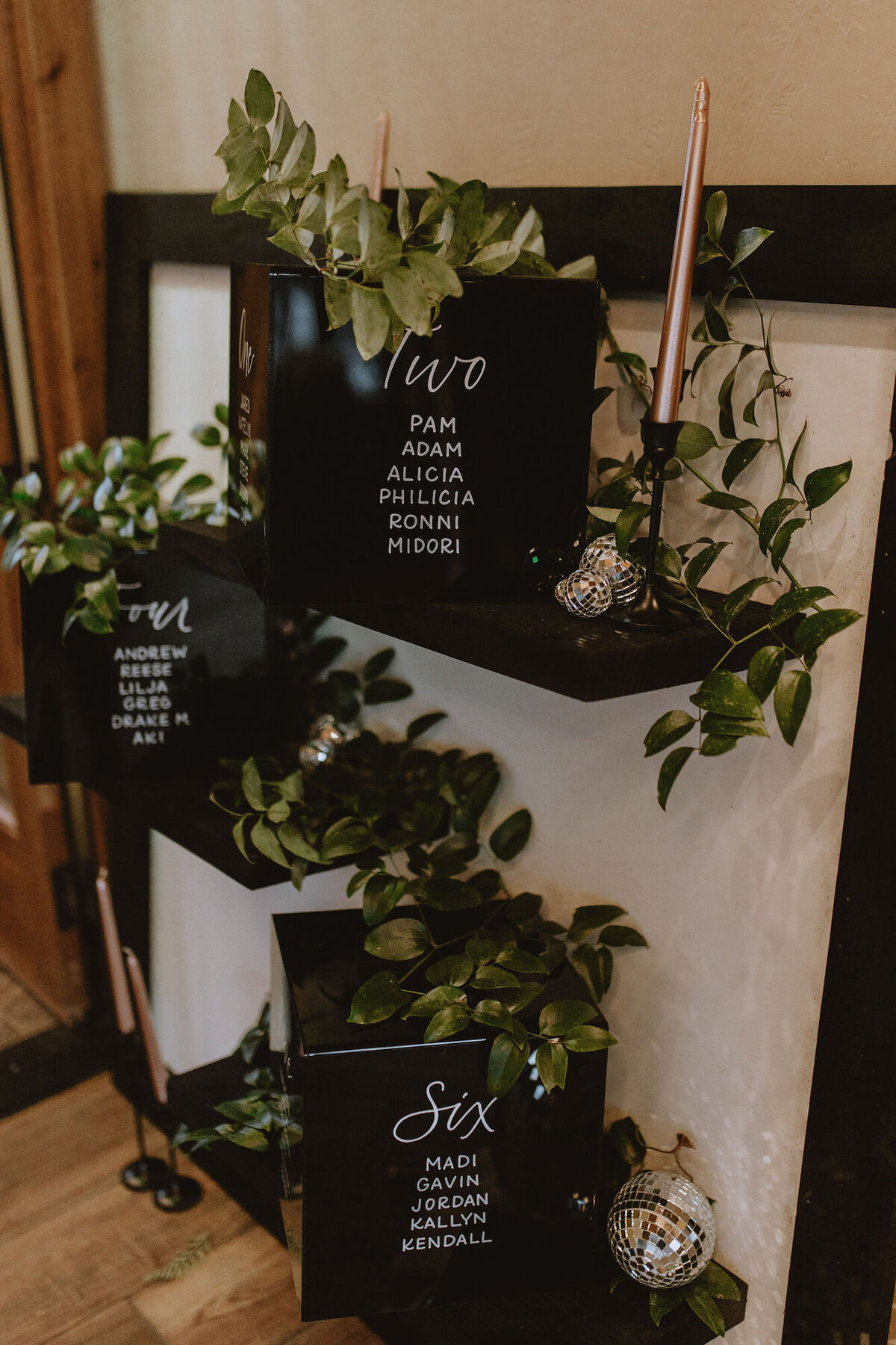Calligraphy seating chart decorated with greenery and disco balls for a microwedding