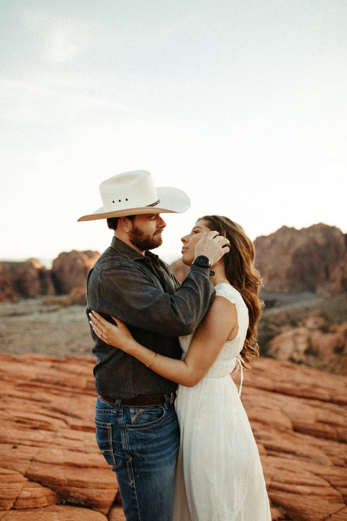Guy in cowboy hat pulling back his fiancé's hair in the desert