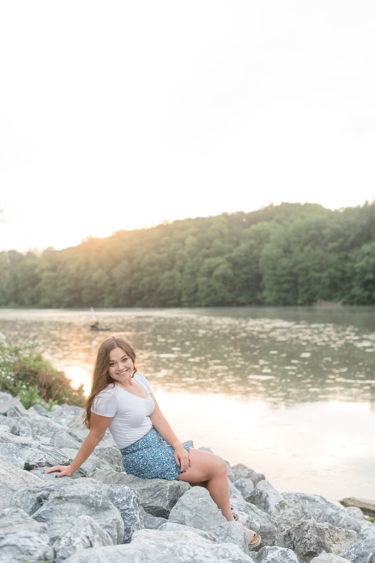 Senior girl sitting on large gray rocks leaning back on right hand at Speedwell Forge Lake in Lititz, Pennsylvania.