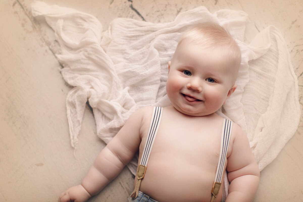 Baby boy on cream background with suspenders on