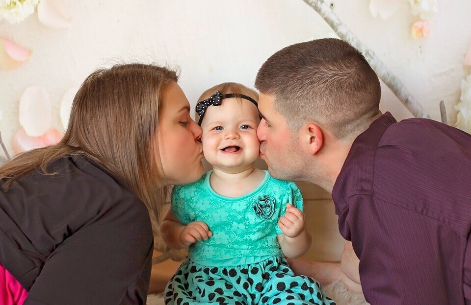 A picture of my husband and I kissing our daughter on the cheeks.