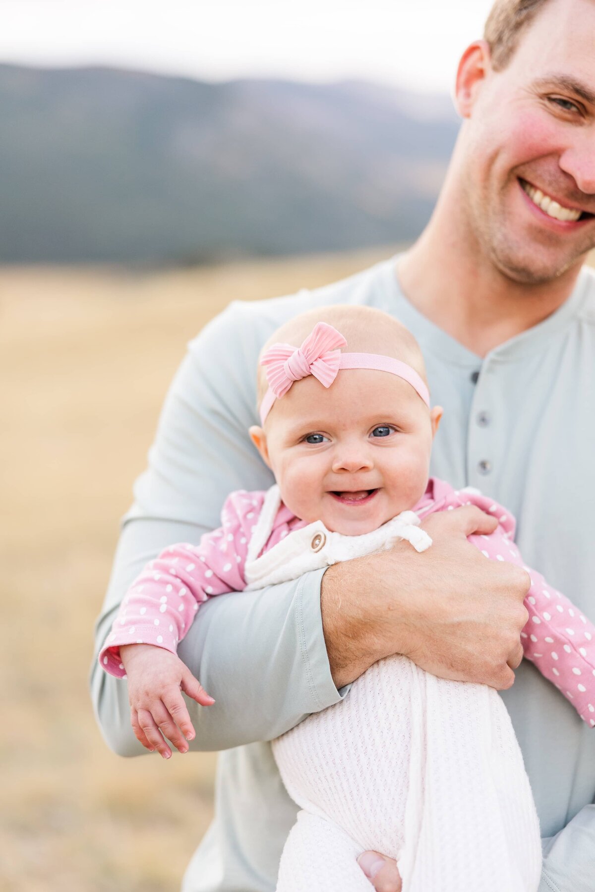 baby girl is smiling at camera while dad holds her in Moraine Park