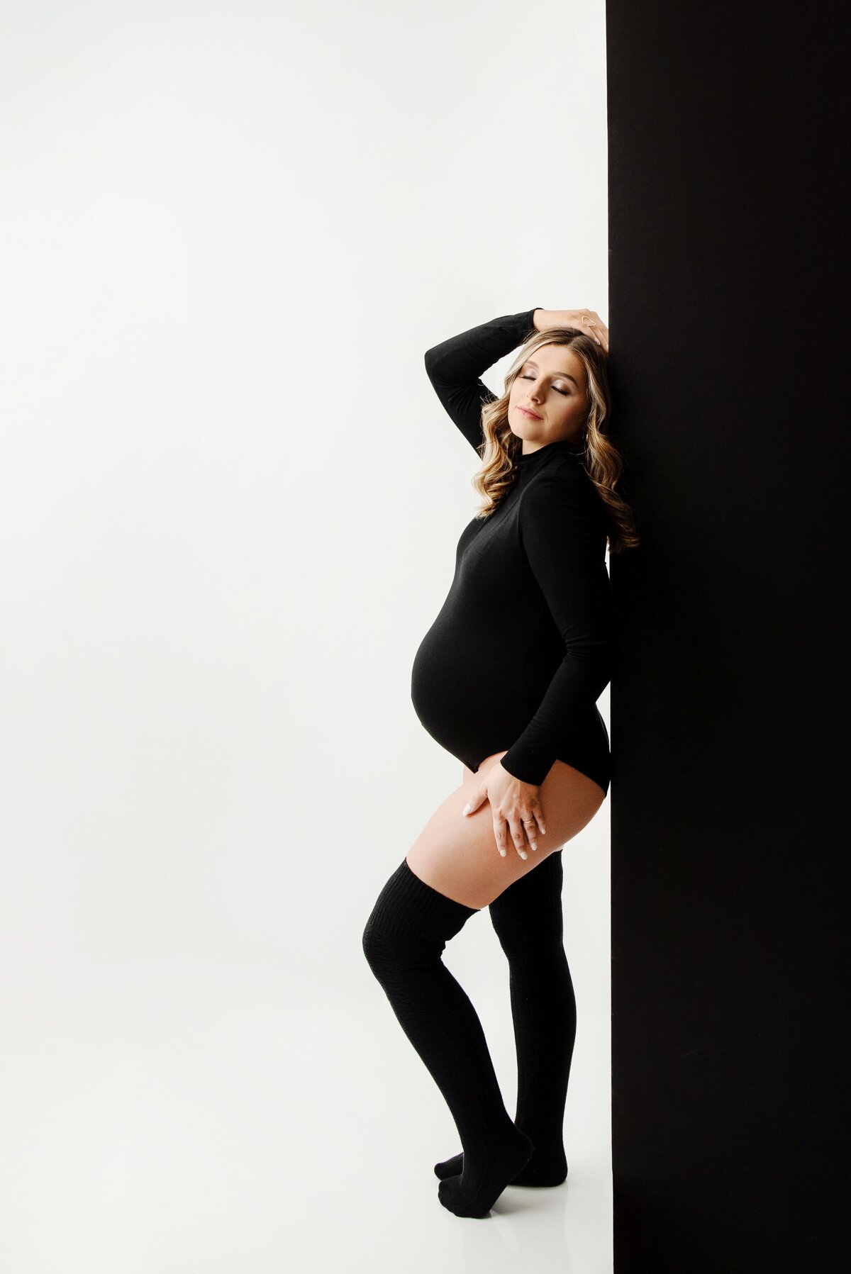 st-louis-maternity-photographer-pregnant-mom-in-black-bodysuit-and-high-socsks-with-black-and-white-wall