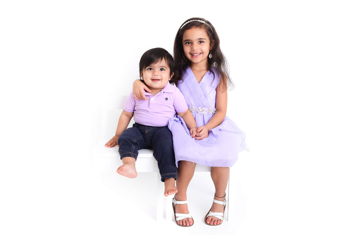 a big sister and baby brother wear light purple and smile at the camera during their family photoshoot