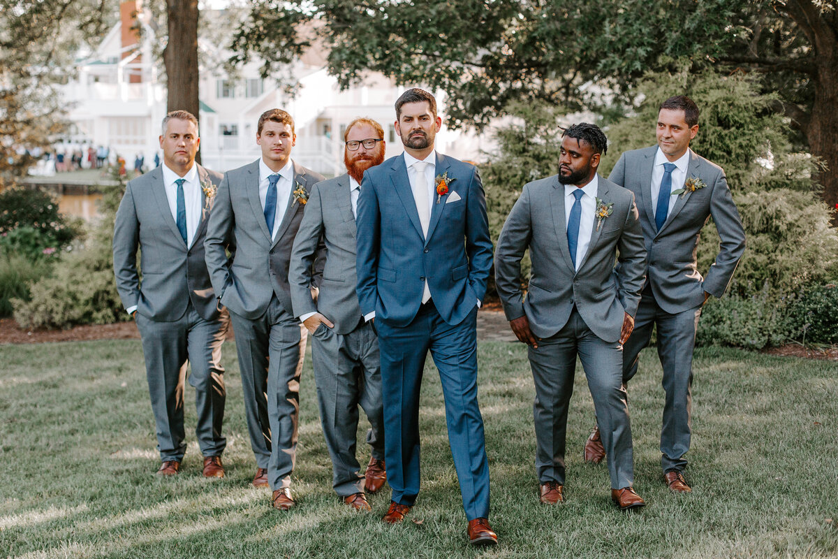 A groom is surrounded by his groomsmen as they stand in a v formation. They are all walking towards the camera