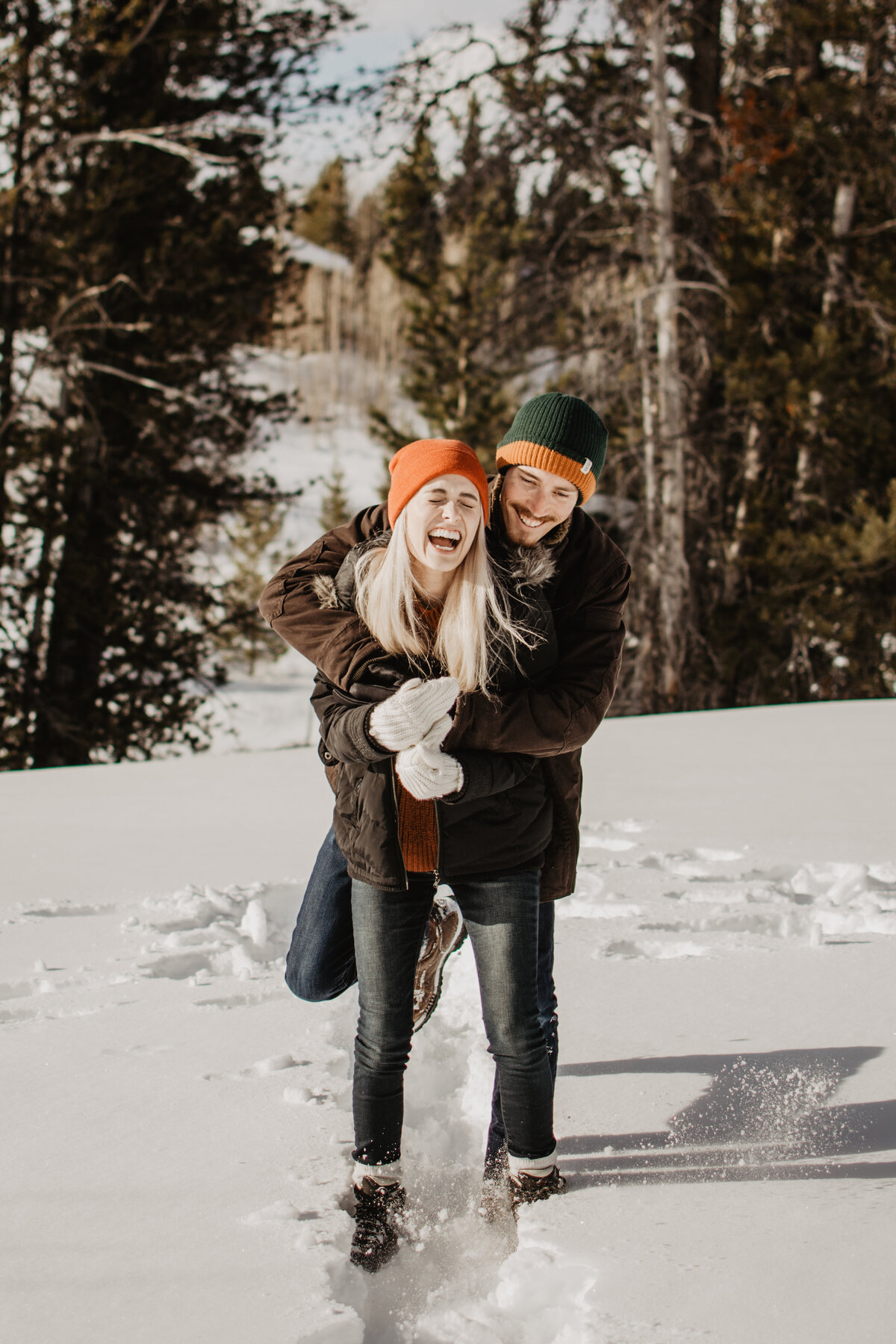 winter engagement pictures with jackson hole photographers photographing man wraps his arms around his fiance during their winter engagement session in Jackson Hole Wyoming as they both laugh