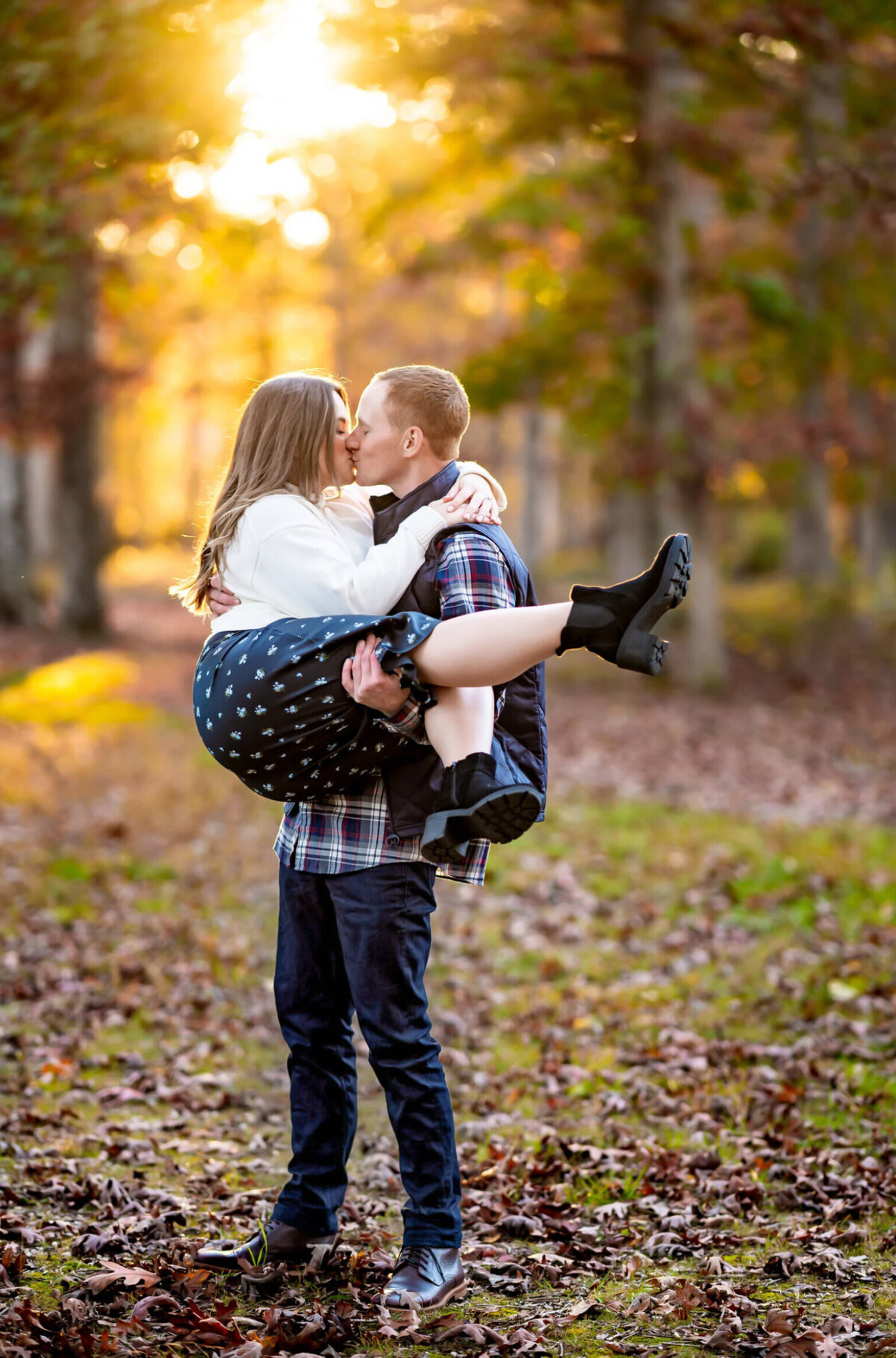 Man, carrying a woman as they kiss in front of the sunlight at Sunset in Allaire State Park