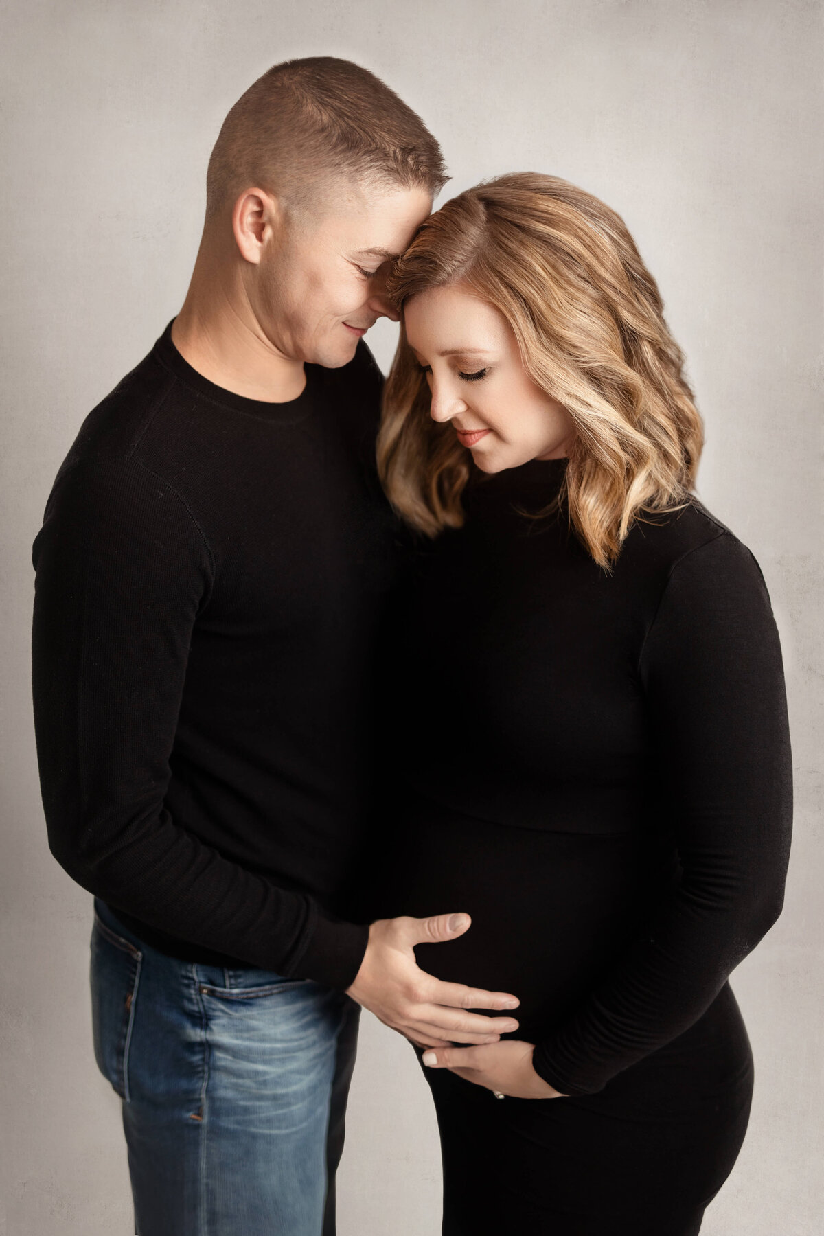 pregnant mom in a black dess looking down at her belly while he husband looks down holding her baby bump