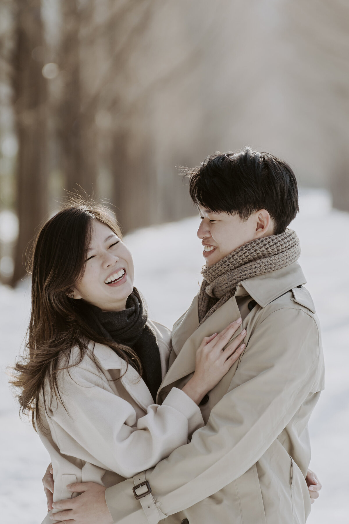 the couple laughing while hugging in metasequoia road full of snow during winter