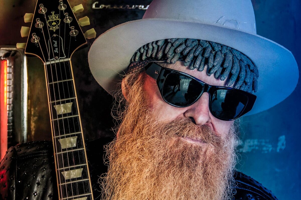 Billy F Gibbons musician portrait close up wearing hat and sunglasses neck of guitar next to his face