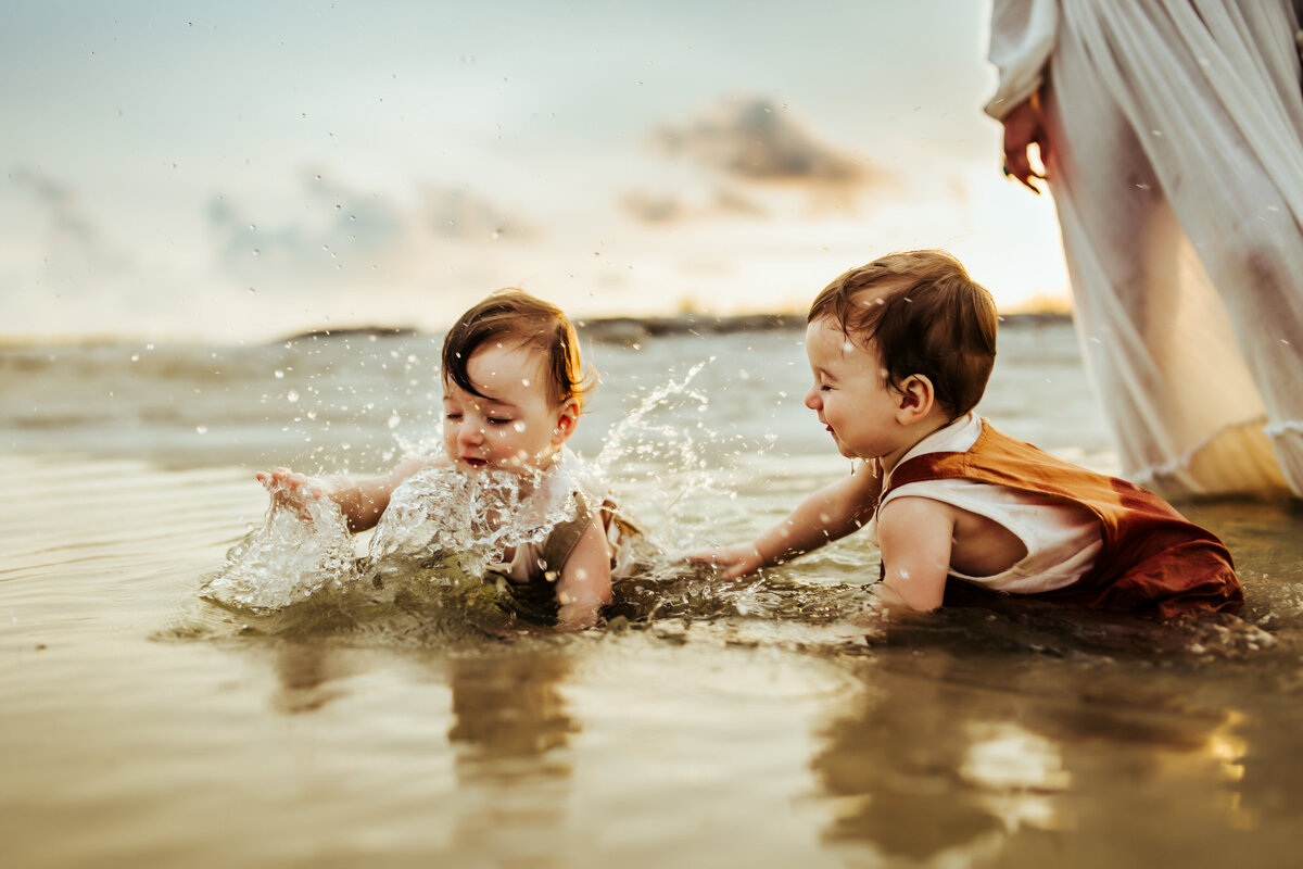twin boys playing in a pool of water at the beach at sunset during a vintage styled family photo session